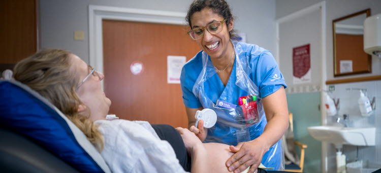 En gravid kvinna ligger i en sjukhussäng samtidigt som hon blir undersökt av en sjuksköterska.