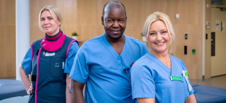 En gruppbild på medarbetare med olika yrken i en korridor och tittar in i kameran.