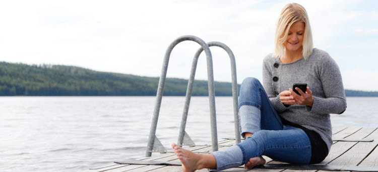 Kvinna sitter på brygga och tittar på sin mobil.